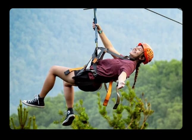 Woman enjoying a high zipline ride at Adventure Park surrounded by lush green hill views
