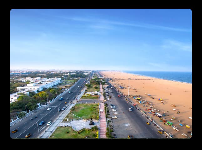 A wide coastal view of Chennai’s Marina Beach with sandy shores, green spaces, and bright blue skies