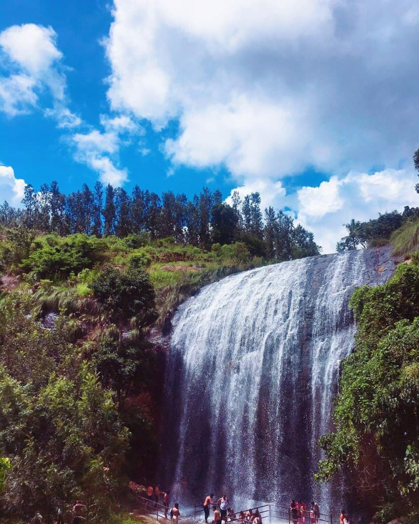A tall waterfall flowing over rocky cliffs surrounded by lush green forests, located minutes away from RushCliff.
