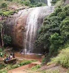 A serene waterfall flowing through forested cliffs with visitors enjoying the natural scenic viewpoint