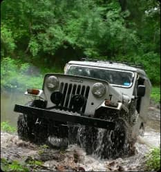 A rugged jeep splashing through a forest stream during an exciting off-road adventure experience
