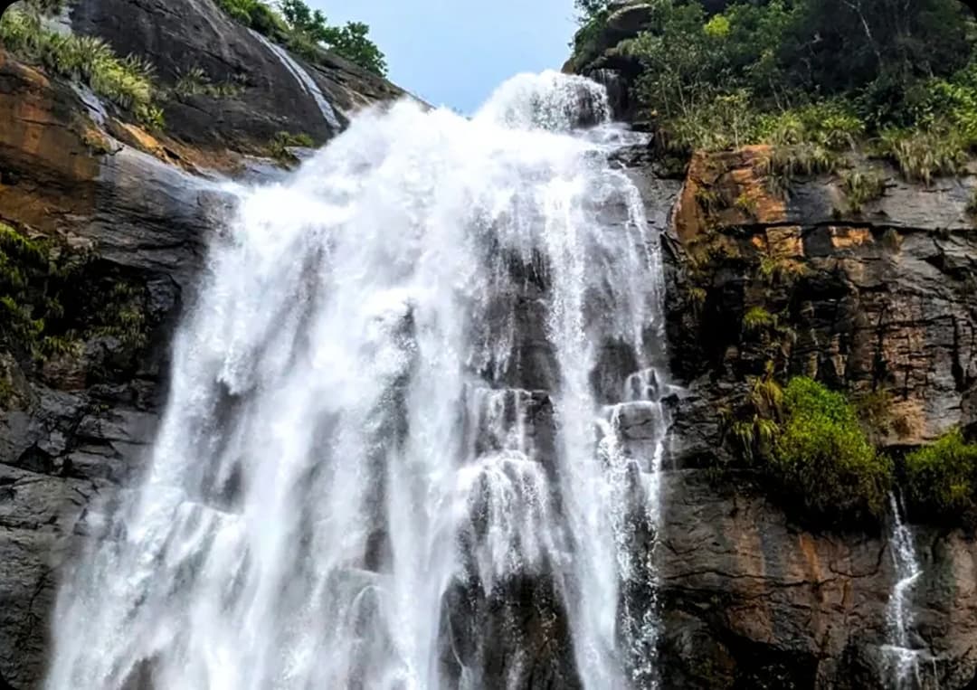 Waterfall cascading down tall rocky cliffs surrounded by lush green vegetation in Kolli Hills