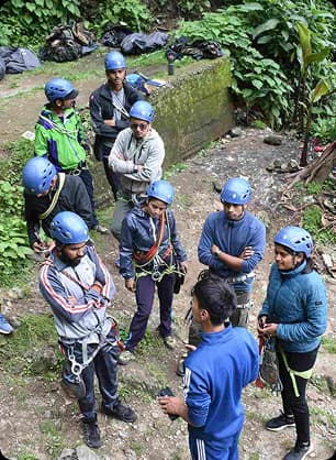 Teen participants wearing helmets gather outdoors for a safety briefing and group formation activity.
