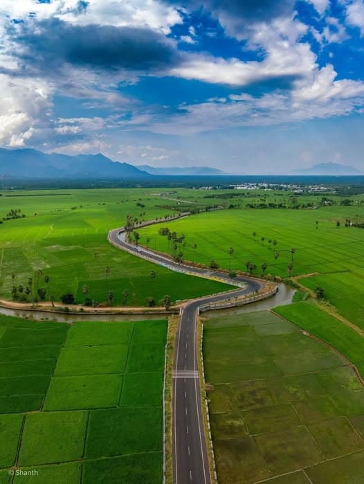 Green fields and winding paths near Erode with long stretches of farmland and distant mountain views.
