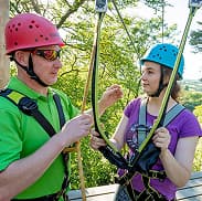 Trained staff assisting students with safety gear during managed adventure activities outdoors.